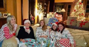 Santa hat, sitting closely together on a couch wearing festive Christmas pajamas in a living room decorated with a lit Christmas tree and presents.